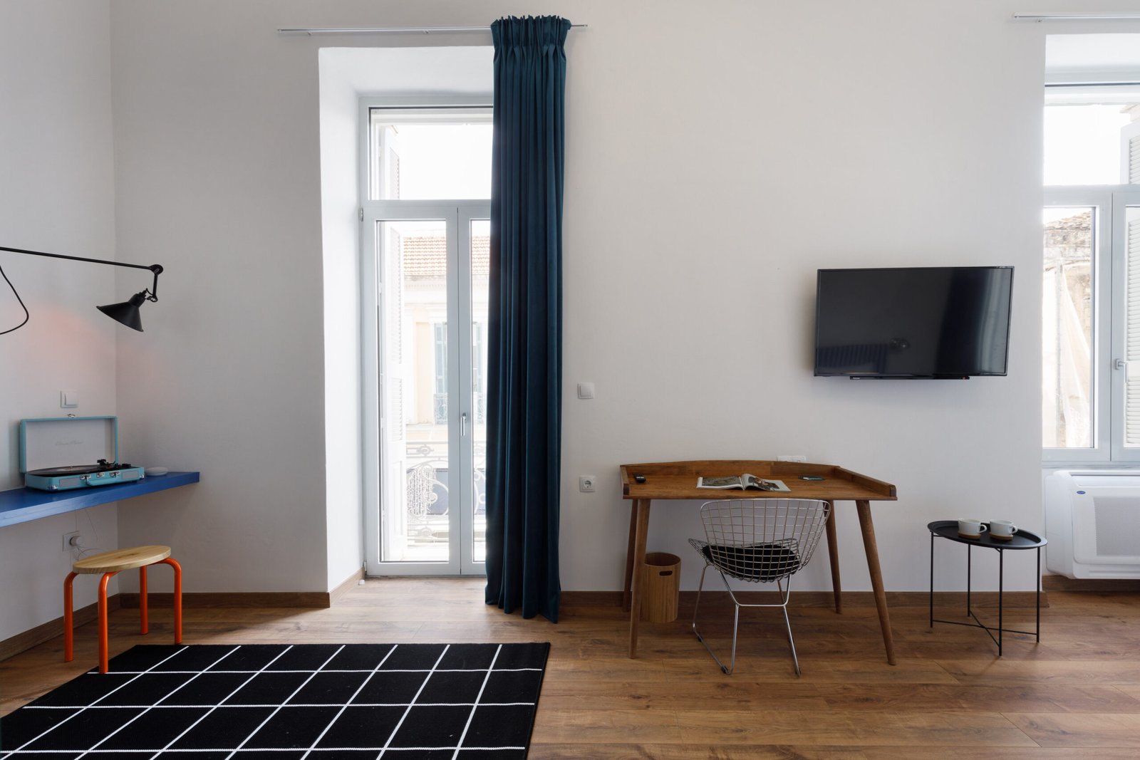 interior of baroness 1 with a tv above the wooden workinf desk, a black and white chess carpet, a wall light and a blue desk with a vinyl player on