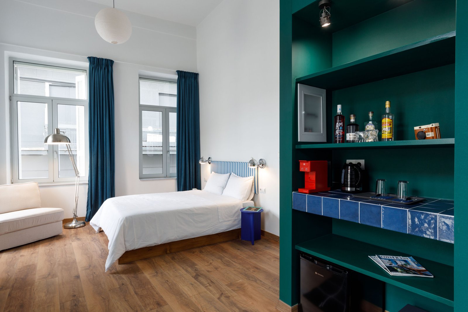 interior of baroness 1 showing the wooden floor, the double wooden bed, a corner white armchair and a green closet with integrated mini bar