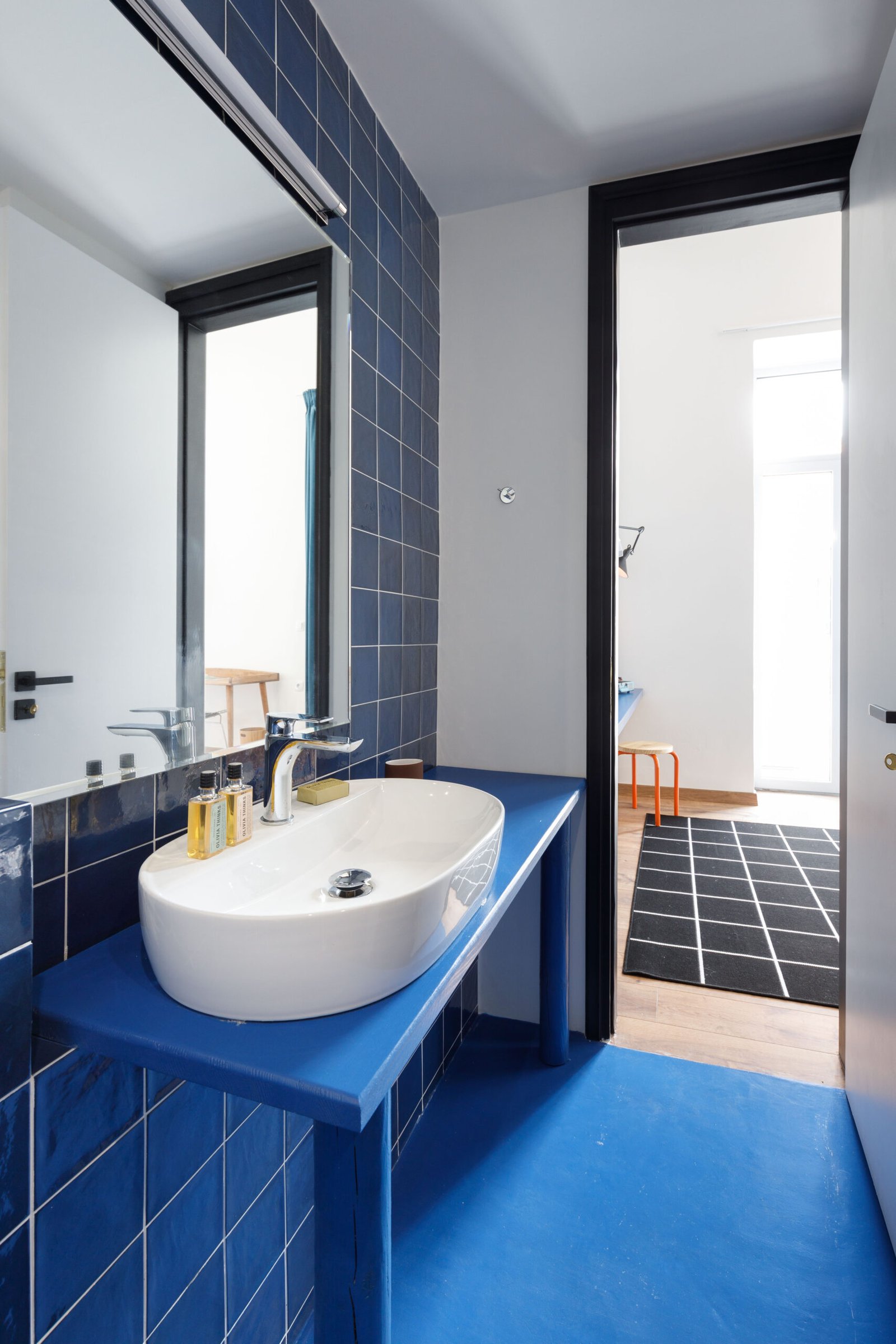 bathroom of baroness 1, with blue tiles, blue floor, big mirror and white sink on blue countertop
