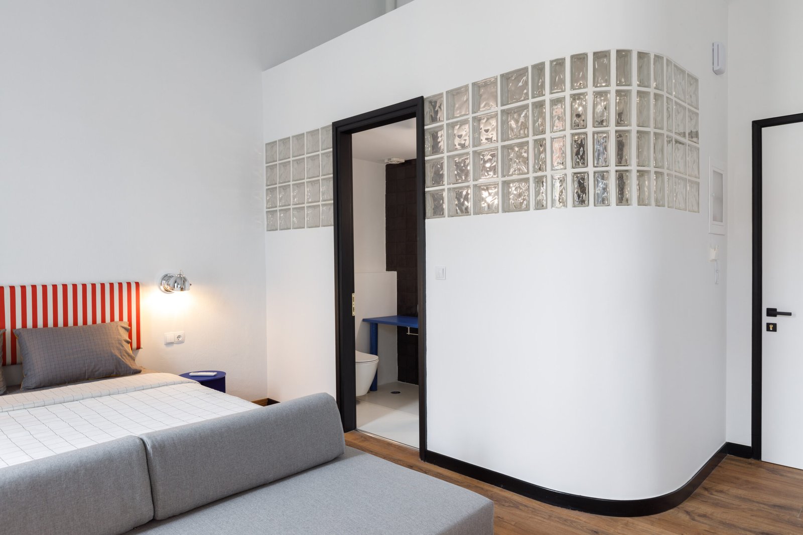 interior of baroness 2 showinf the bed, with the exterior of the bathroom, with white walls, black door and glassbrick