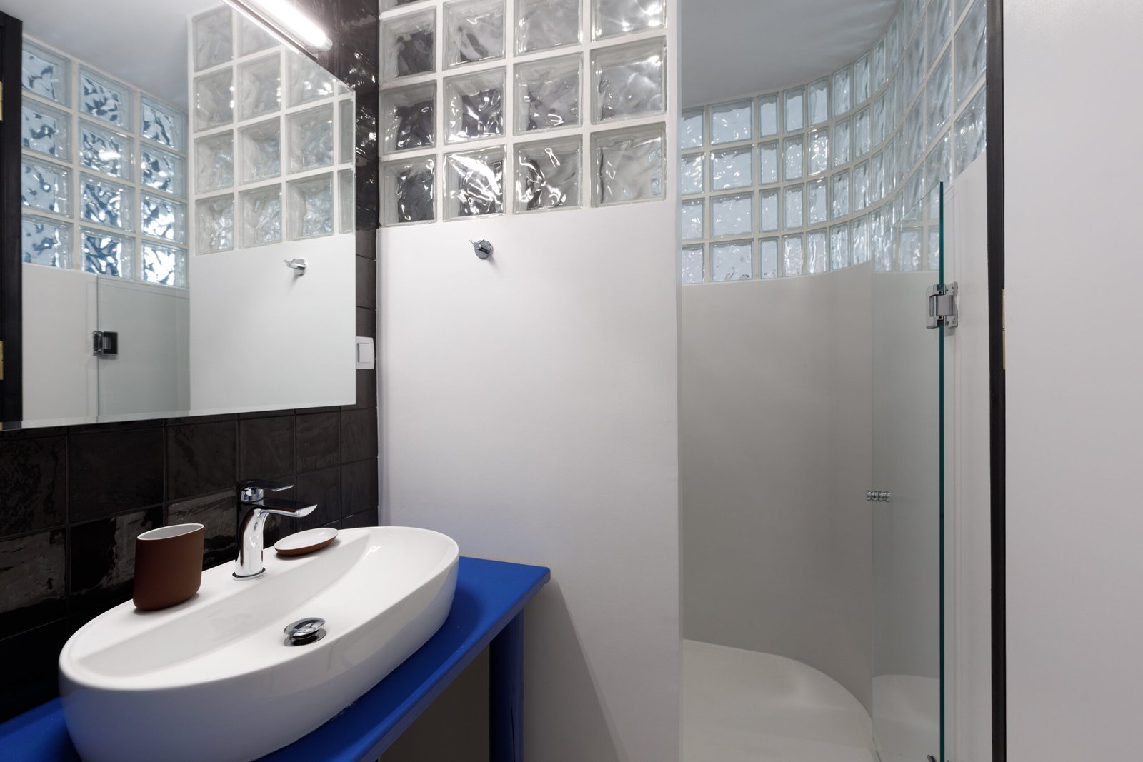 bathroom of baroness 2, with glassbricks at the shower, a mirror above the white sink and a blue countertop