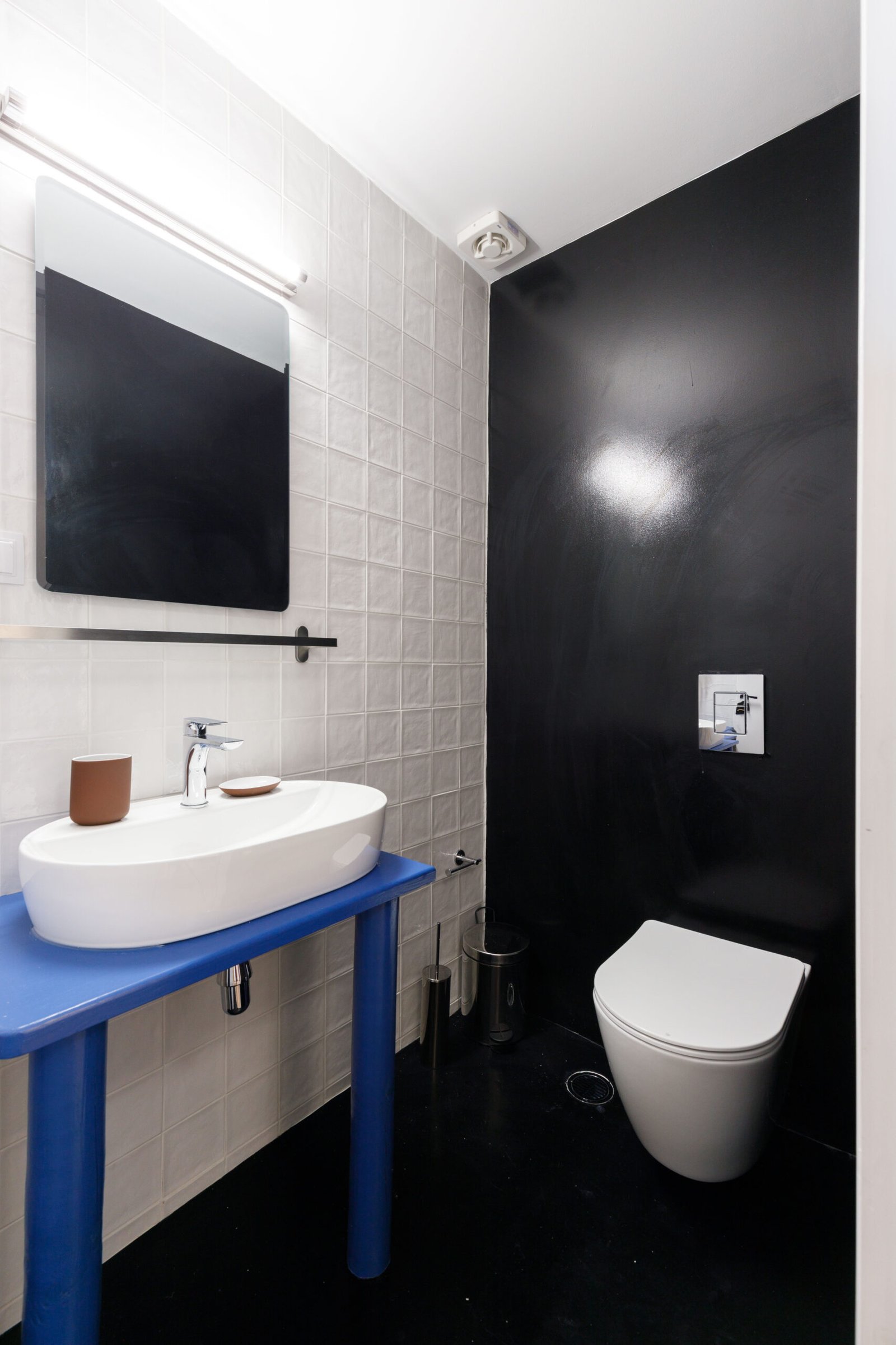 picture from the bathroom of Baroness 2, showing the toilet, the white sink, white tiles, black floor and blue countertop