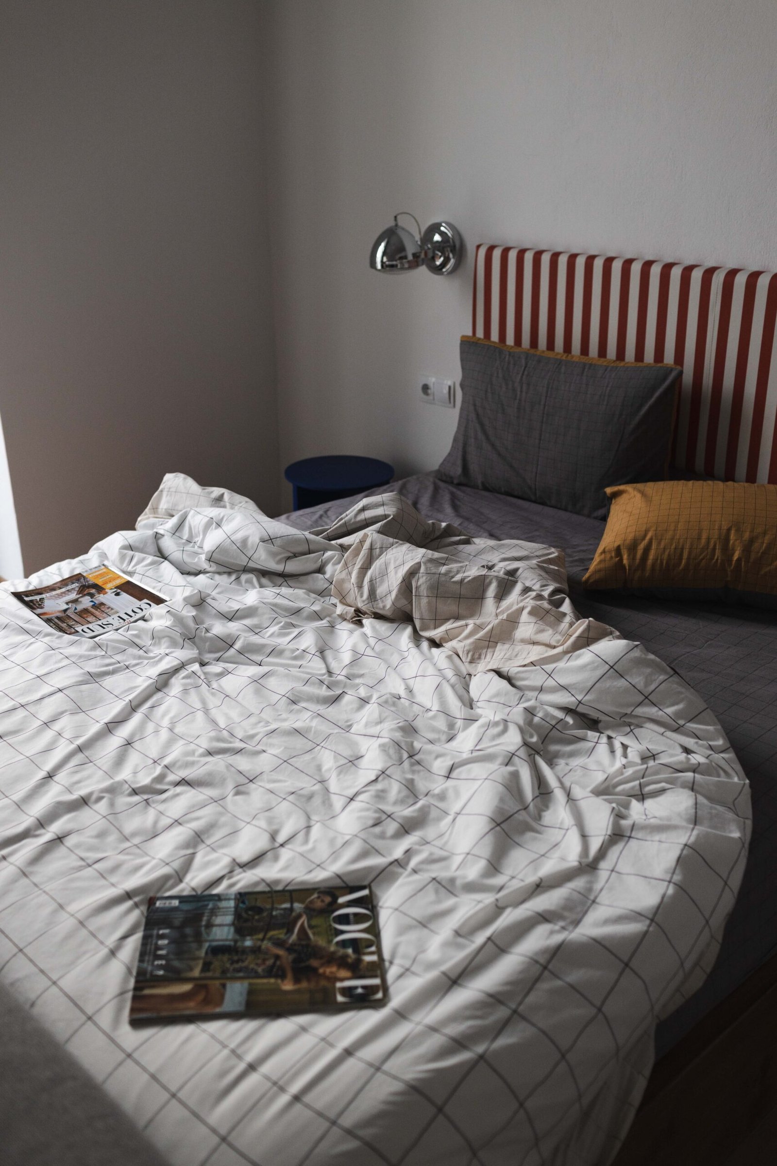 artistic photo of the bed of baroness 2 with messy bed linen, headboard with red and white stripes and a magazine on the sheets