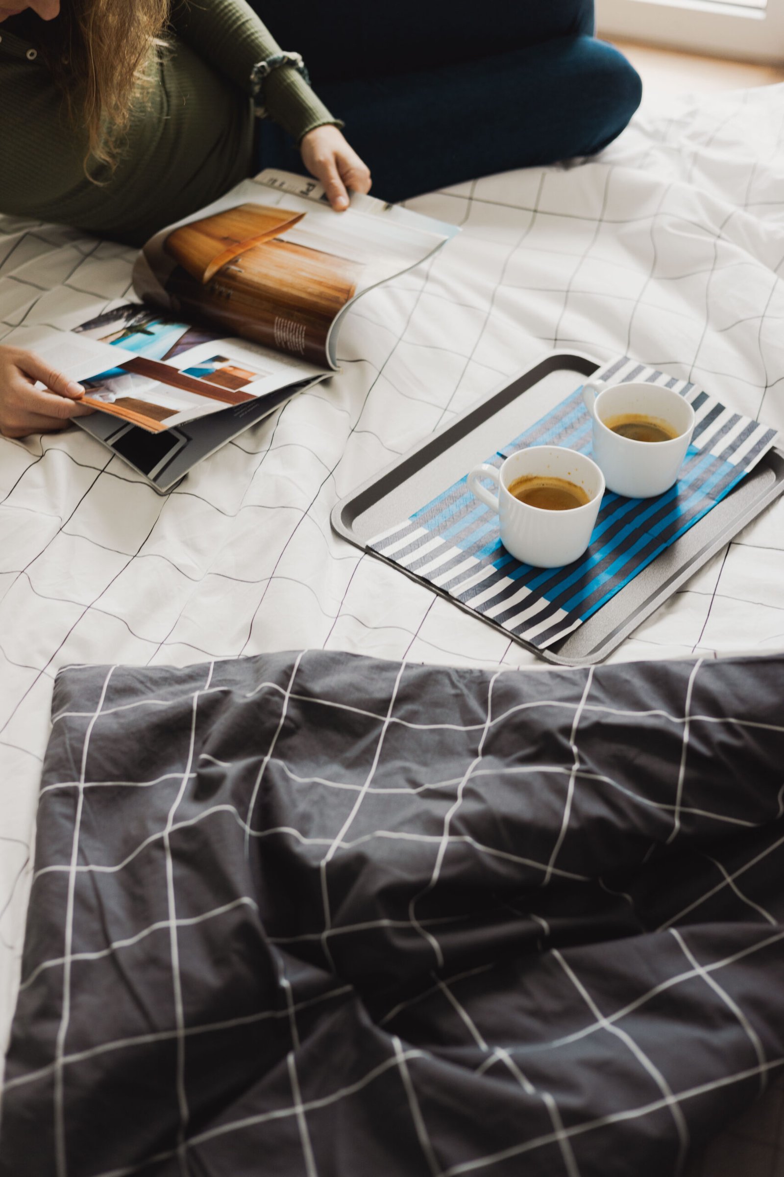 close view to two cups of coffe on black and white sheets, and awoman reading magazines