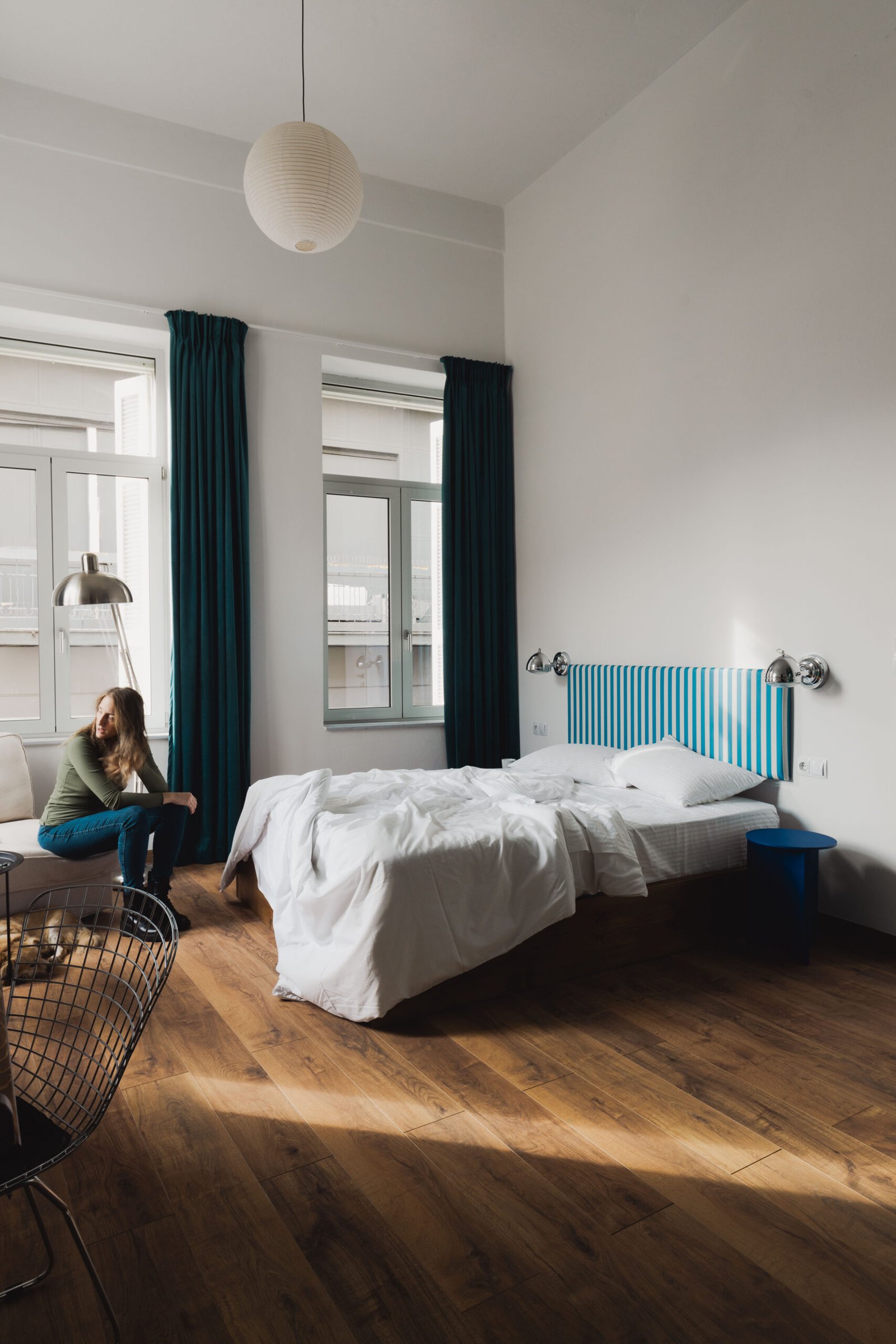 το δωματιο του baroness 1, με το διπλο κρεββατι, ξυλινο δαπεδο, και μια γυναικα να καθεται στην γωνιακη, λευκη πολυθρονα